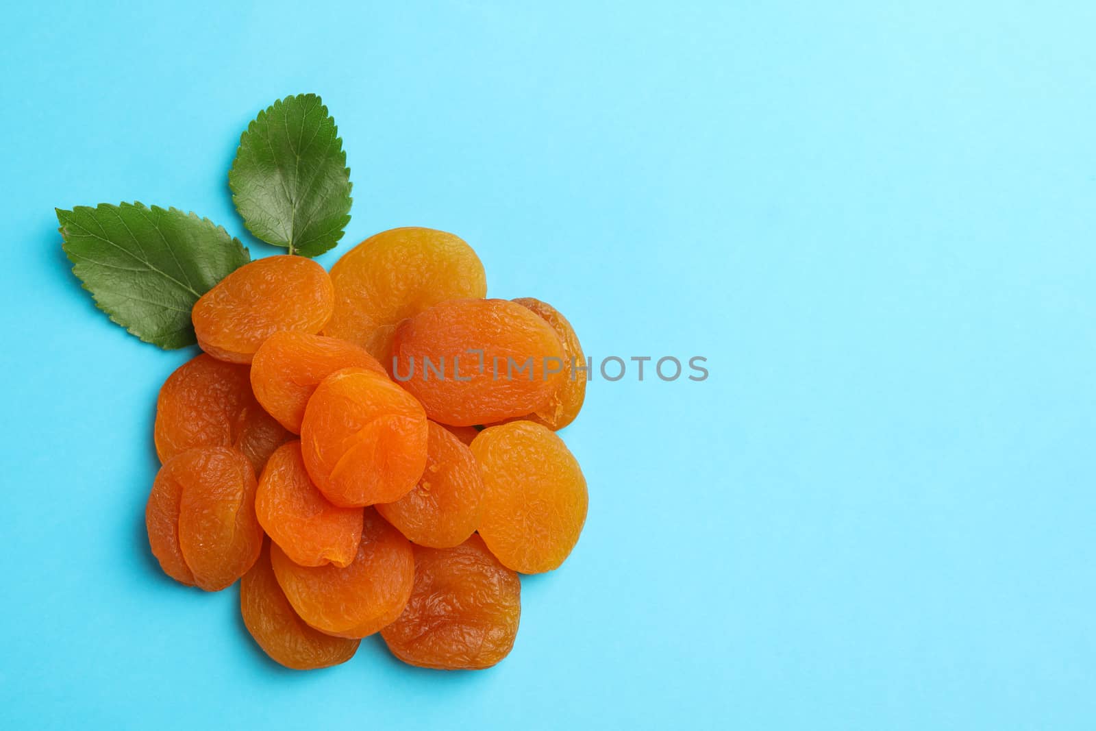 Tasty dried apricot and leaves on blue background