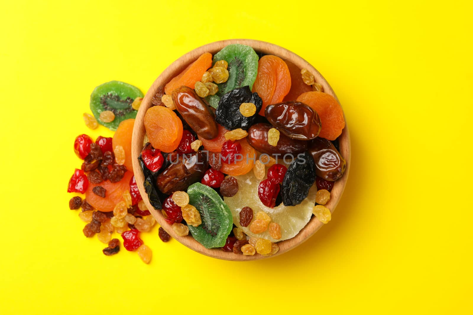 Wooden bowl with dried fruits on yellow background