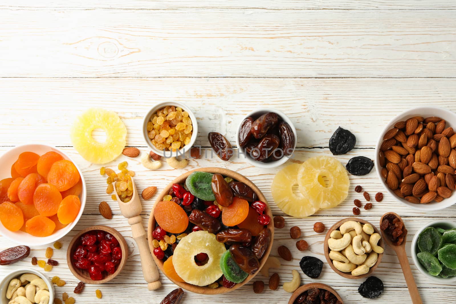 Bowls with dried fruits and nuts on white wooden background