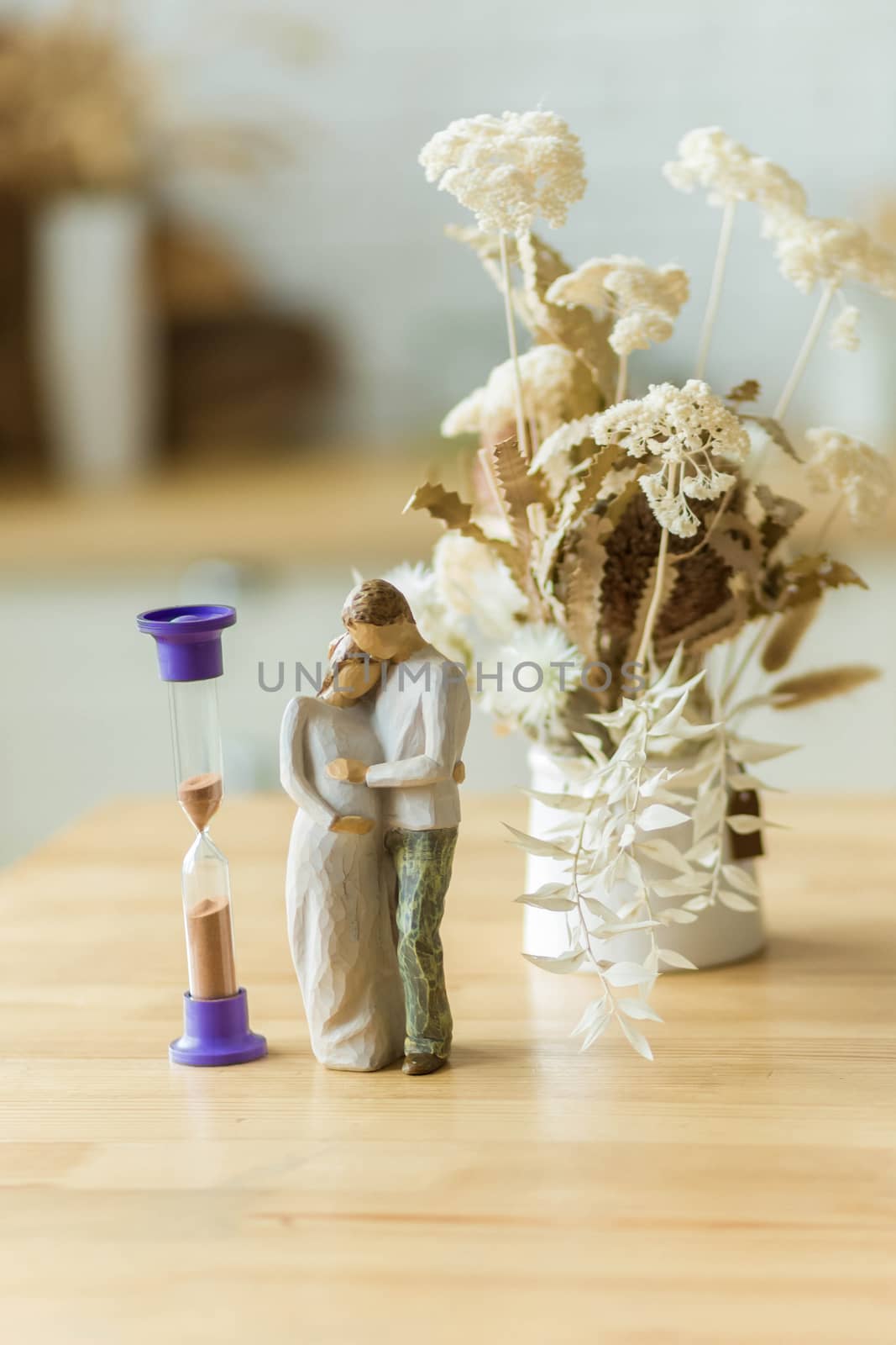 .Dried flowers in a vase on the dining table next to the hourglass and the statuette of the parents. Time is running out, manage to become parents