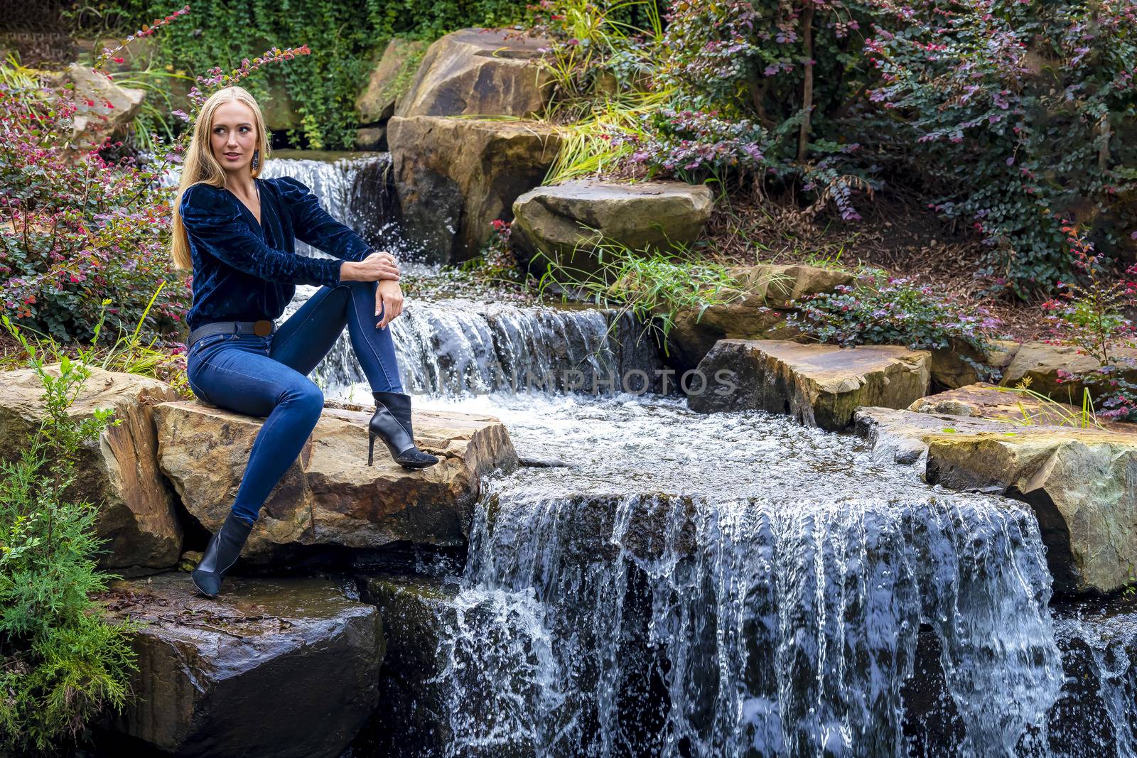 A gorgeous blonde model sits near a waterfall at a local park
