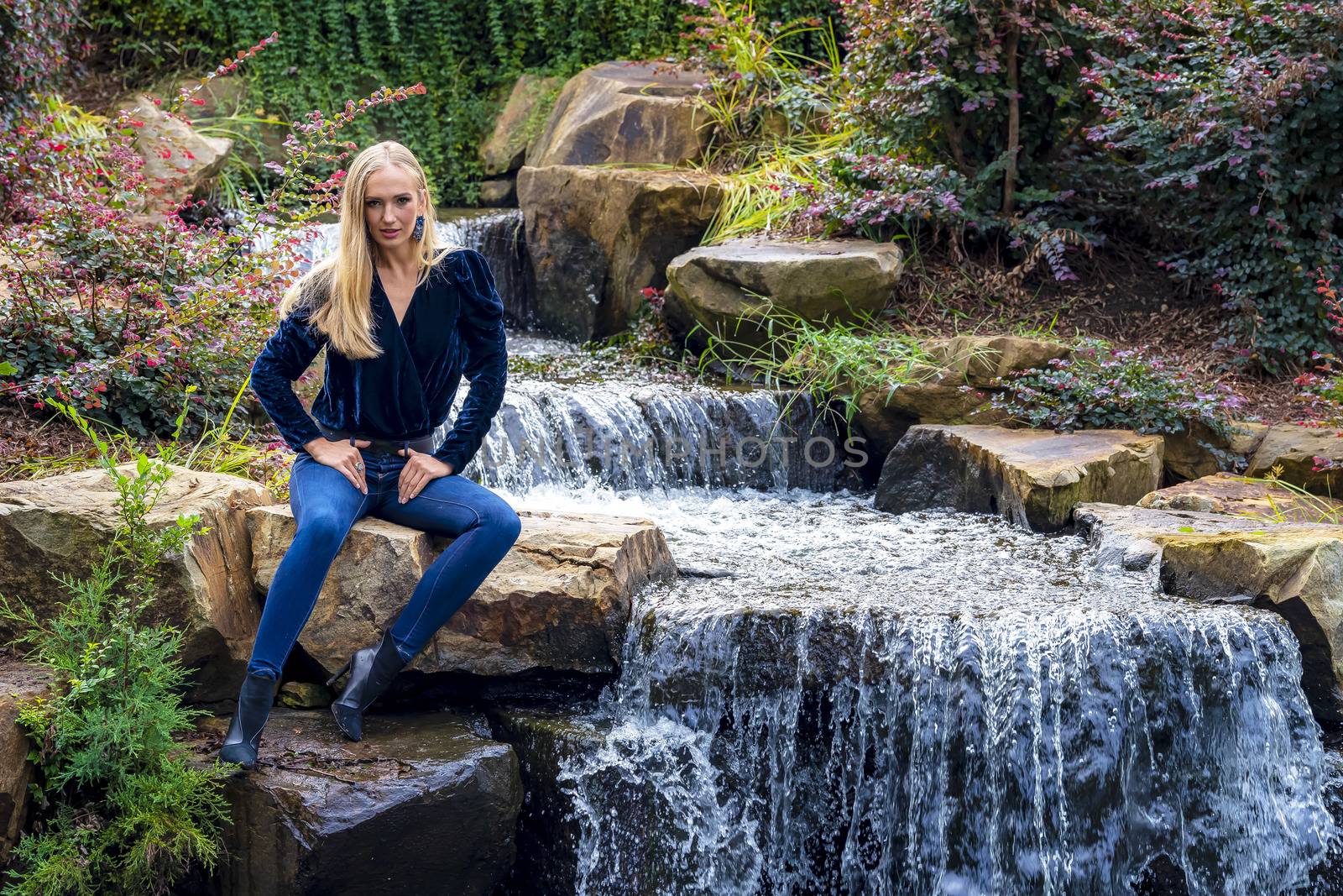 A gorgeous blonde model sits near a waterfall at a local park