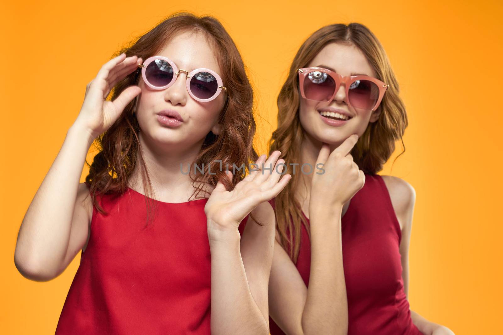 Happy sisters in red dresses on a yellow background are having fun and gesticulating Copy Space by SHOTPRIME