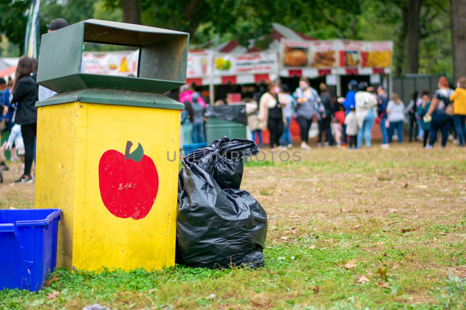 A Yellow Trash Can at a Carnival With an Apple Painted on It