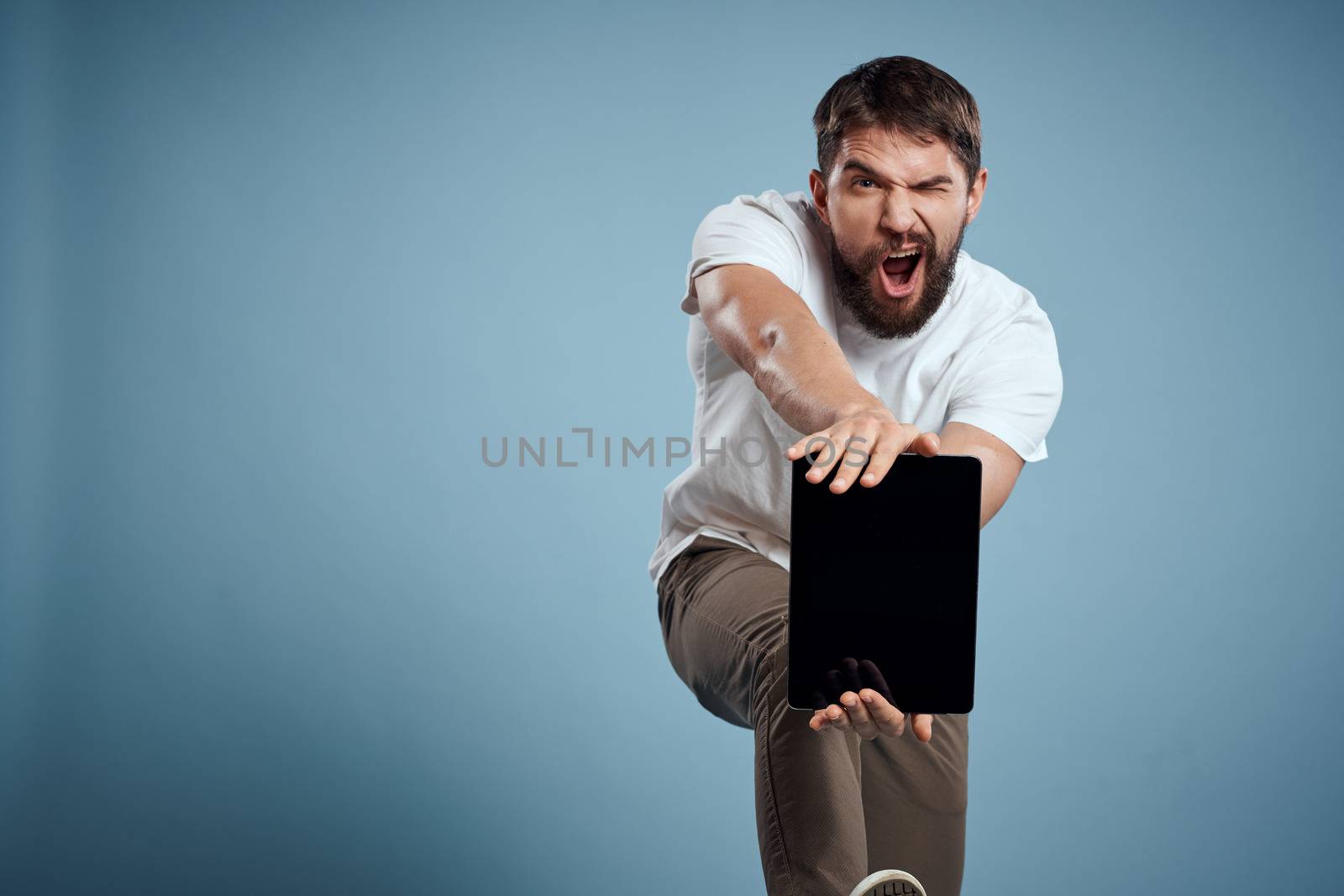 Energetic man with a touch tablet on a blue background in a white t-shirt cropped view. High quality photo