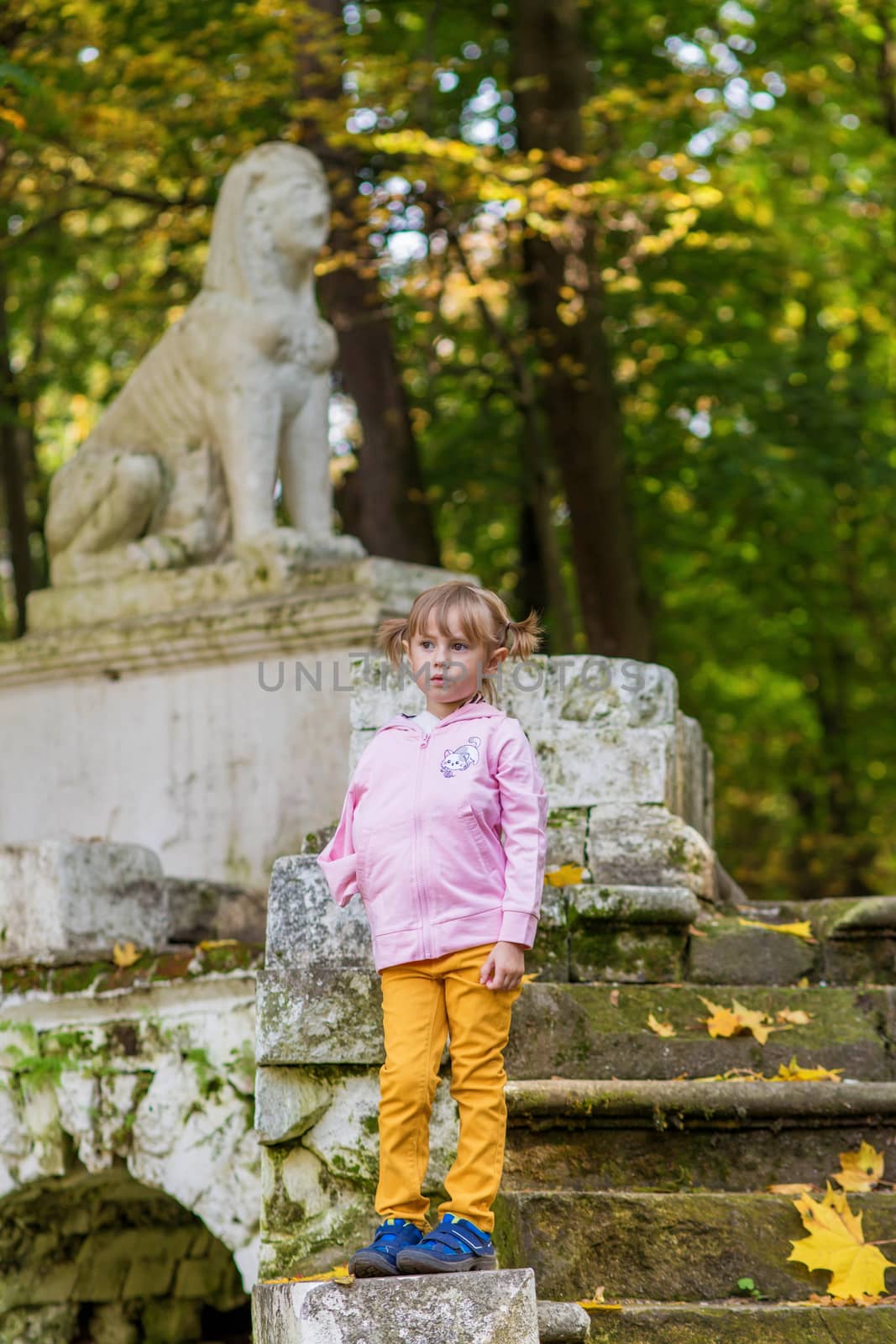 A girl with a broken arm stands on the stairs in an old park on an autumn walk