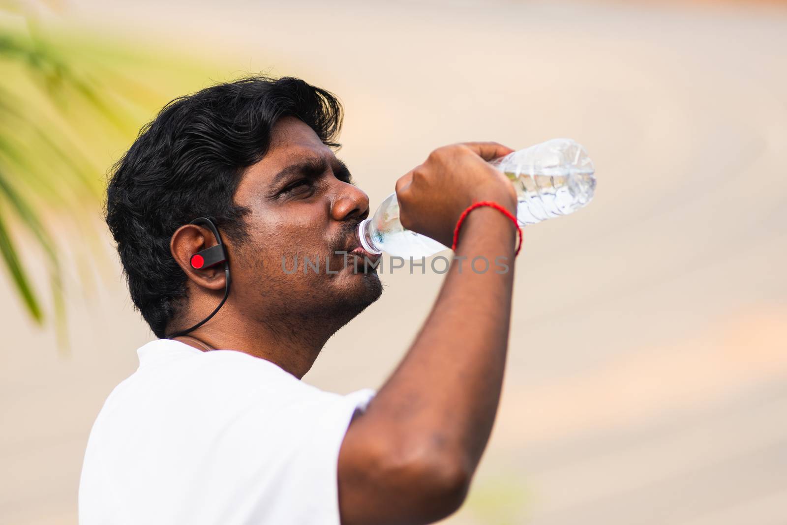 Close up Asian young sport runner black man wear athlete headphones he drinking water from a bottle after running at the outdoor street health park, healthy exercise workout concept