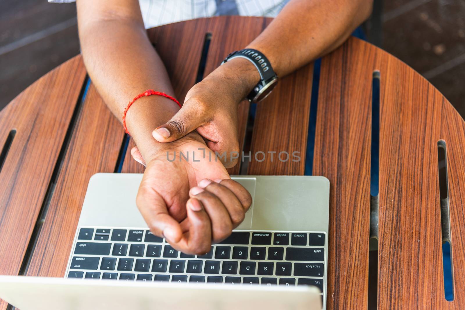 Closeup hands the Asian black man holding his wrist pain from using laptop computer he working long time, Injury office syndrome hand pain by occupational disease concept