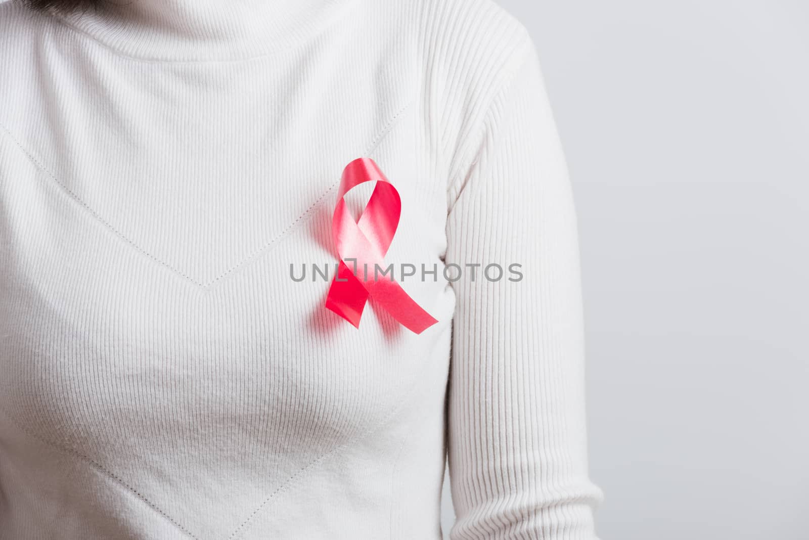 Breast cancer awareness healthcare and medicine concept. Close up Asian woman wear white shirt standing with pink breast cancer awareness ribbon pin on chest, studio shot isolated on white background