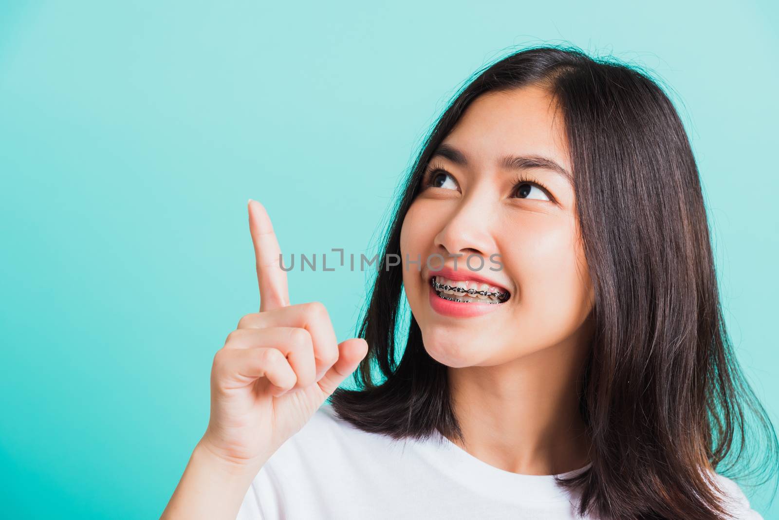 Portrait of Asian teen beautiful young woman smile have dental braces on teeth laughing point finger side away blank copy space, studio shot isolated on blue background, medicine and dentistry concept