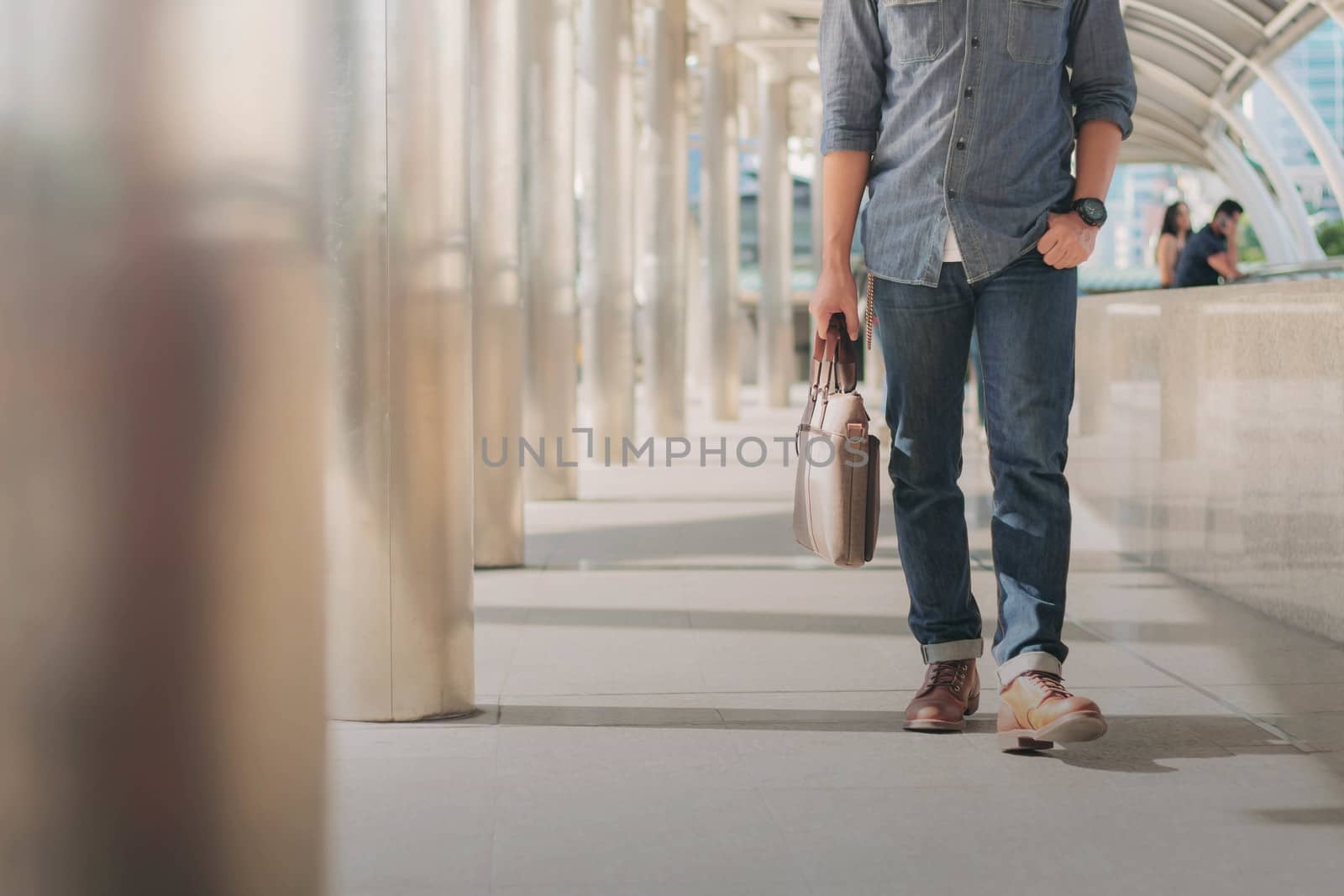 Young man with blue jeans walking carrying leather bag in the city.