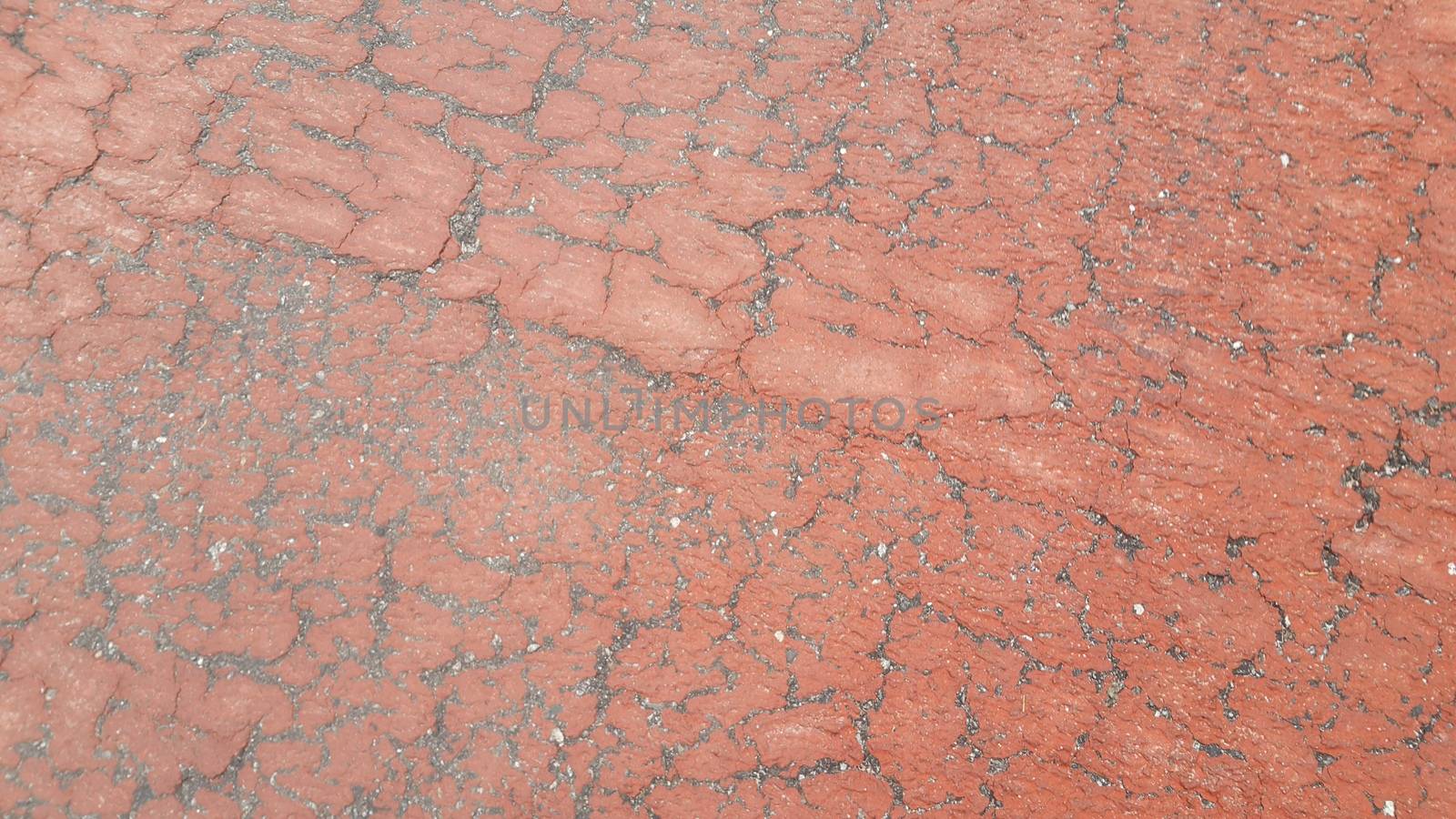 Red colored damaged road or paved pathway with crackes of different shpaes. Cracked texture with copy space for text and messages