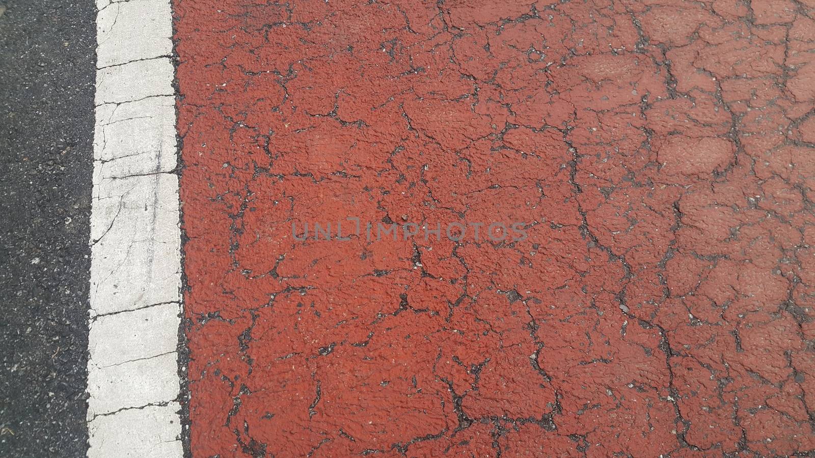 Red colored damaged road or paved pathway with crackes of different shpaes. Cracked texture with copy space for text and messages