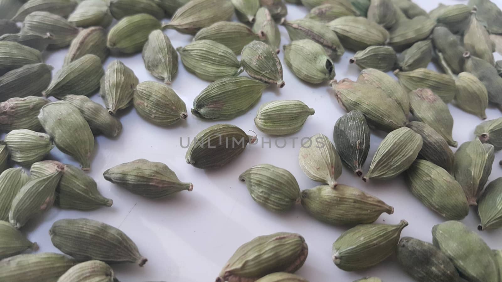 Closeup top view of dried green Elettaria cardamomum fruits with seeds, cardamom spice scattered on white background