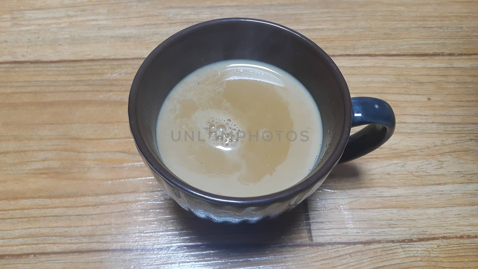 Top view of hot milk tea or black tea in a dark brown ceramic cup placed over a wooden floor.