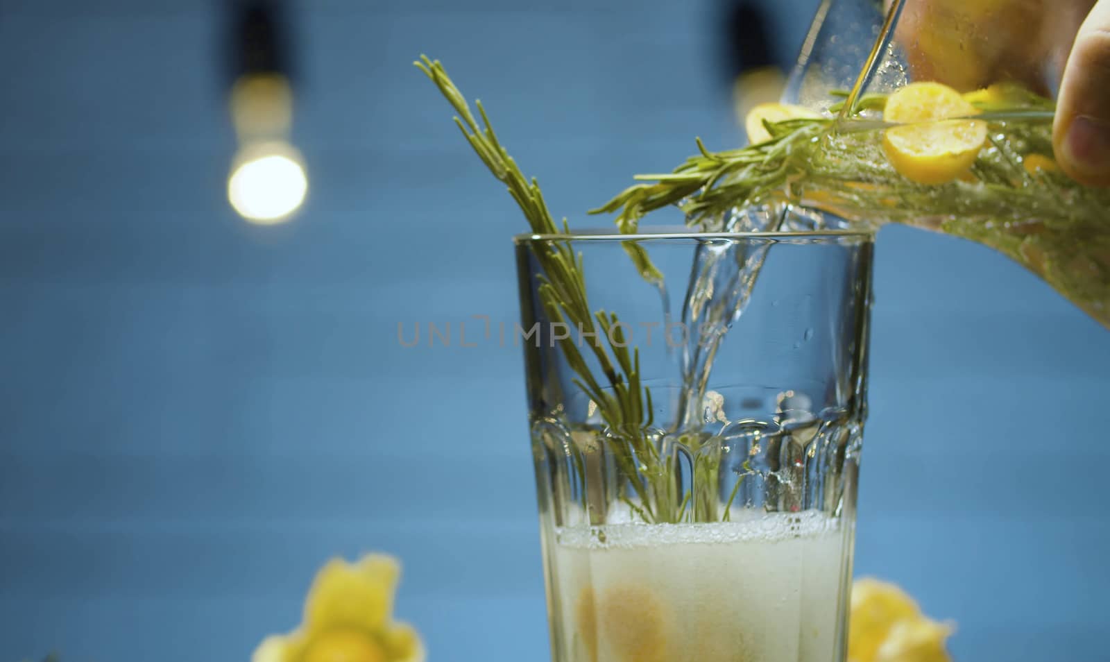 Close up pouring rosemary and physalis fizzy drink into a glass. Blurry lights on blue background