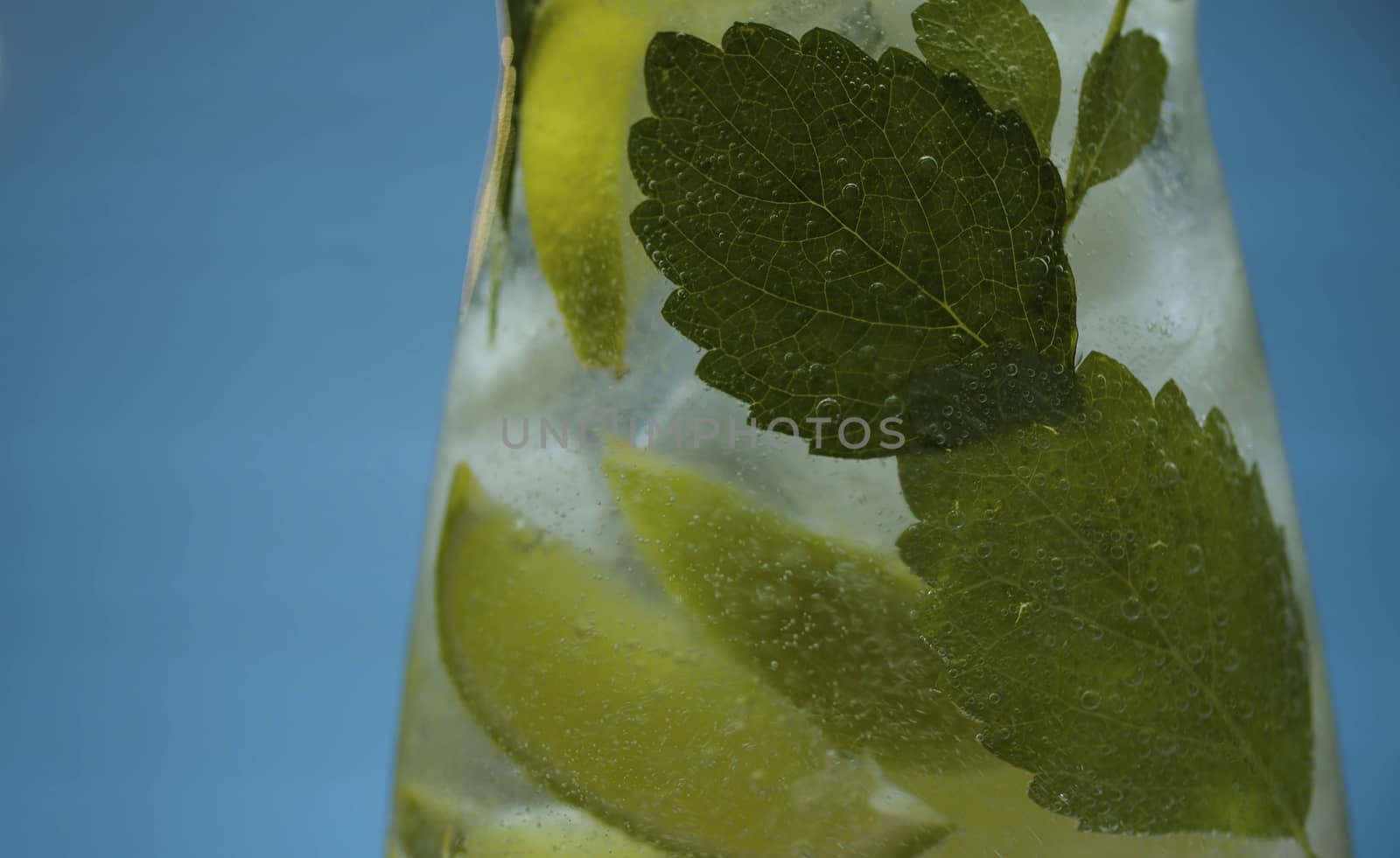 Close up lemonade with lime and mint in glass jug on blue background