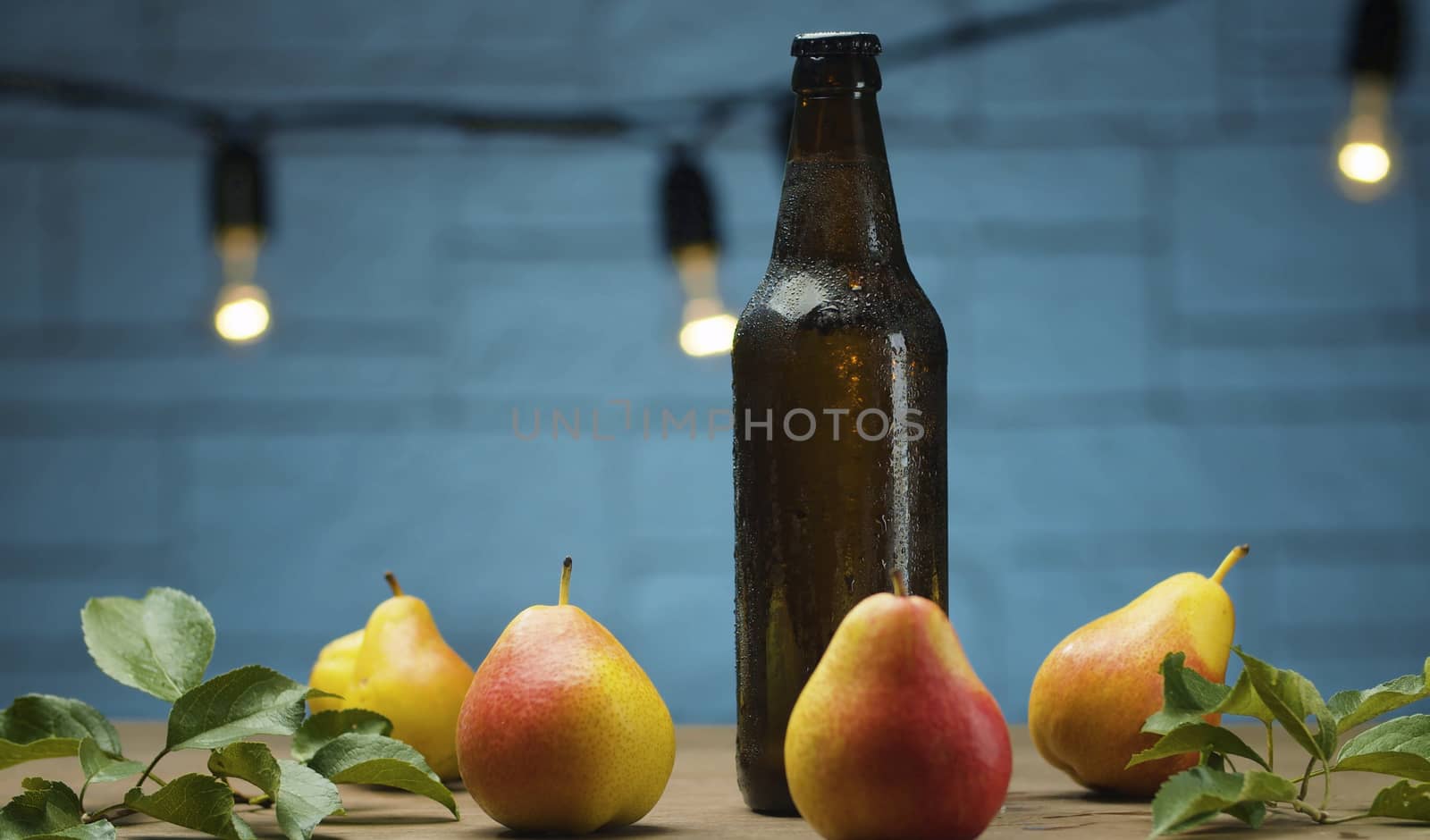 Close up male hand putting misted bottle of cider on the table on blue background. Fresh ripe pears. Healthy food, vitamins, fruits