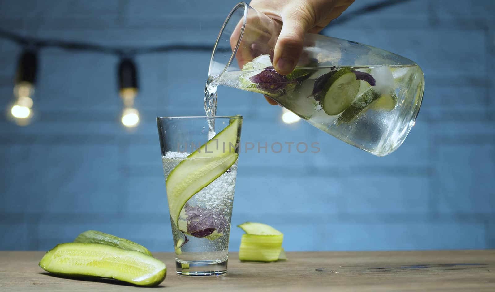 Close up male hand pouring vegetable fizzy drink into a glass. Blurry bulbs on blue background