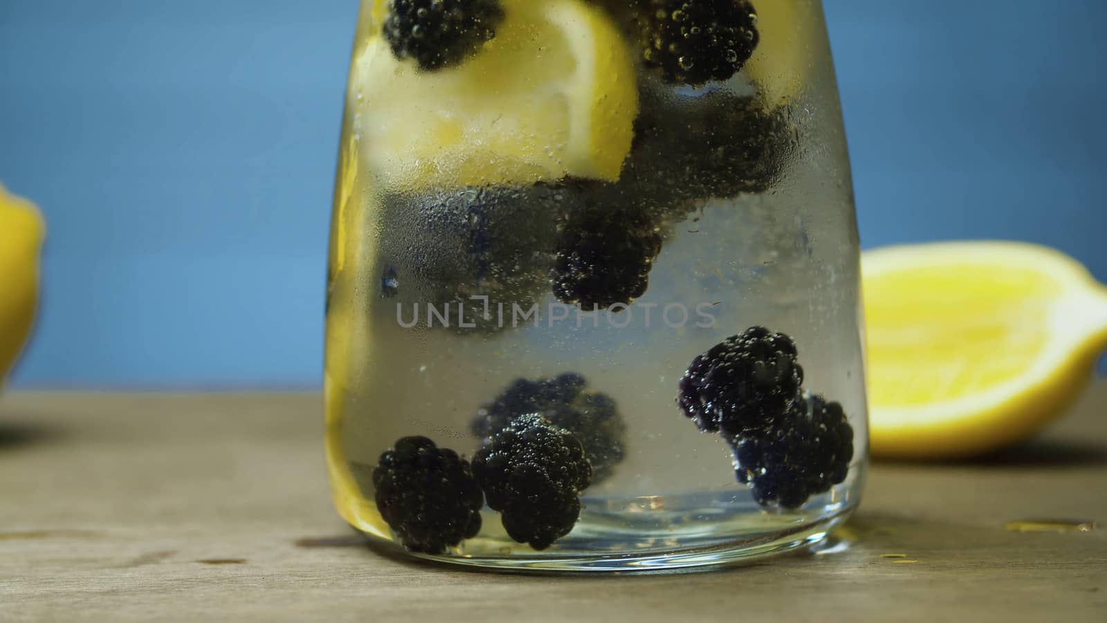 Close up dewberry lemonade in glass jug. Blurry lamps on blue background