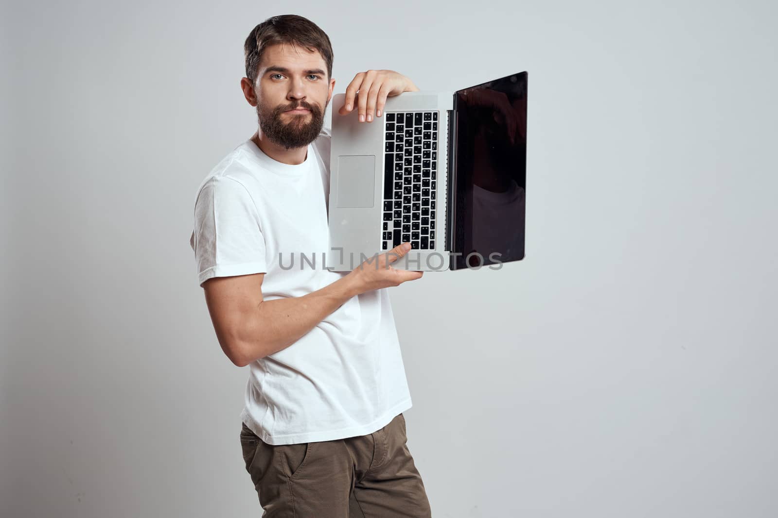 A man with a laptop in his hands on a light background in a white t-shirt emotions light background cropped view model portrait new technologies. High quality photo