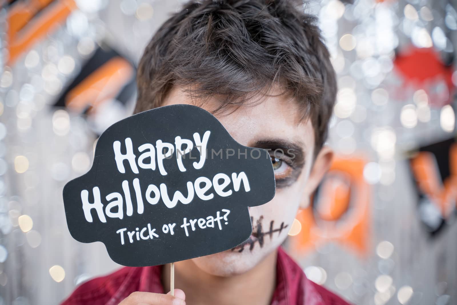Kid hloding Halloween booth prop infront of spooky face - concept of halloween trick or treat