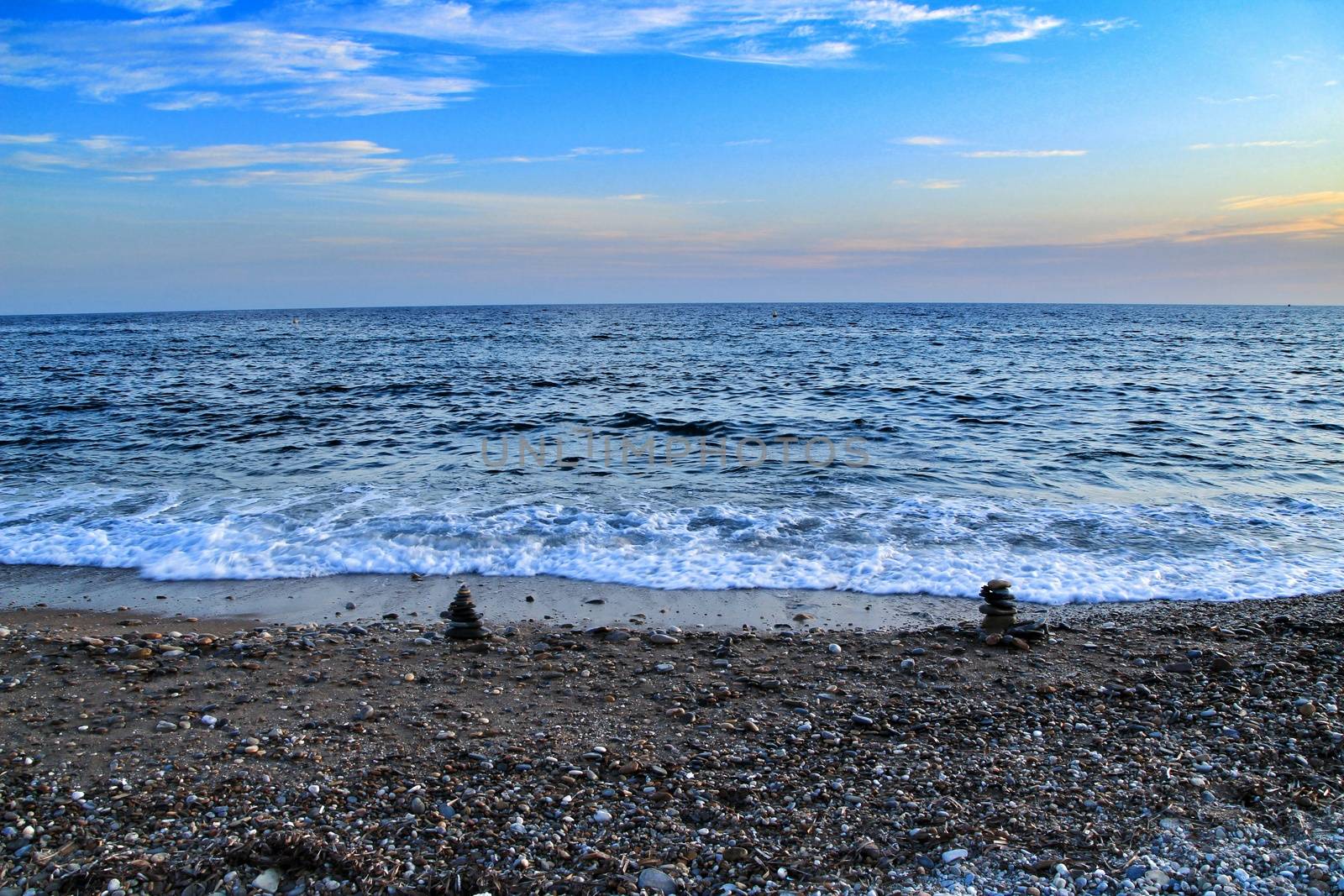 Round stacked stones on the Isla Plana beach at sunset in Cartagena. Waves in the background.