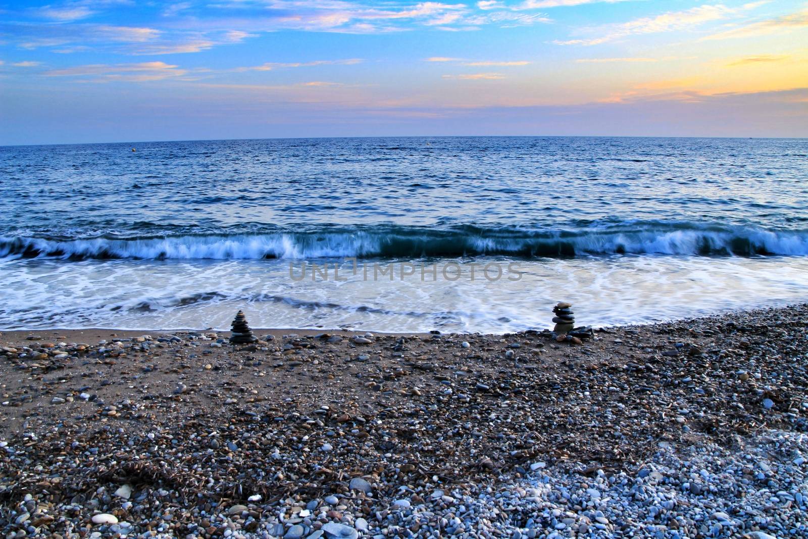 Round stacked stones on the Isla Plana beach at sunset in Cartagena. Waves in the background.