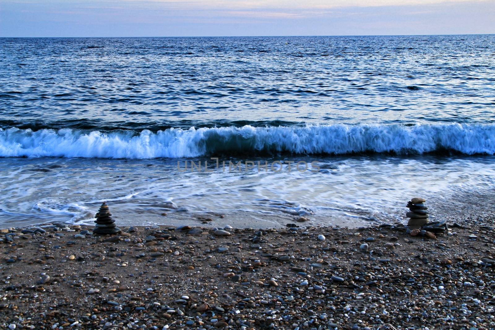 Round stacked stones on the Isla Plana beach at sunset in Cartagena. Waves in the background.