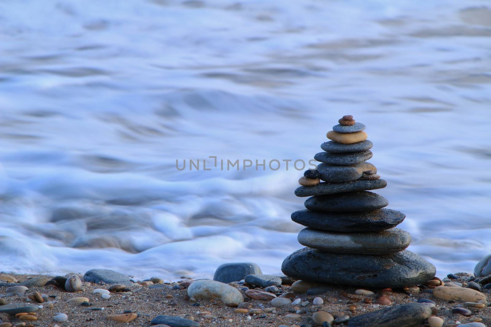 Round stacked stones on the Isla Plana beach at sunset in Cartagena. Waves in the background.