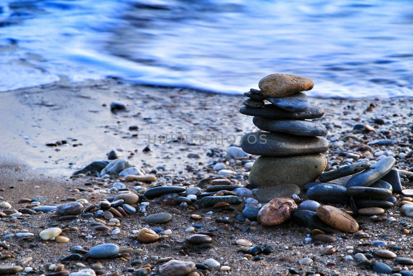 Round stacked stones on the Isla Plana beach at sunset in Cartagena. Waves in the background.