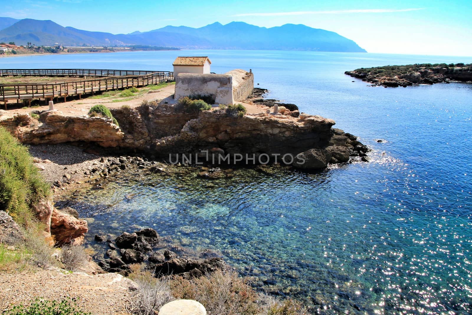 Old thermal baths on the beach with boulders, cliffs and mountains in Isla Plana village in Cartagena, Murcia, Spain in a sunny day