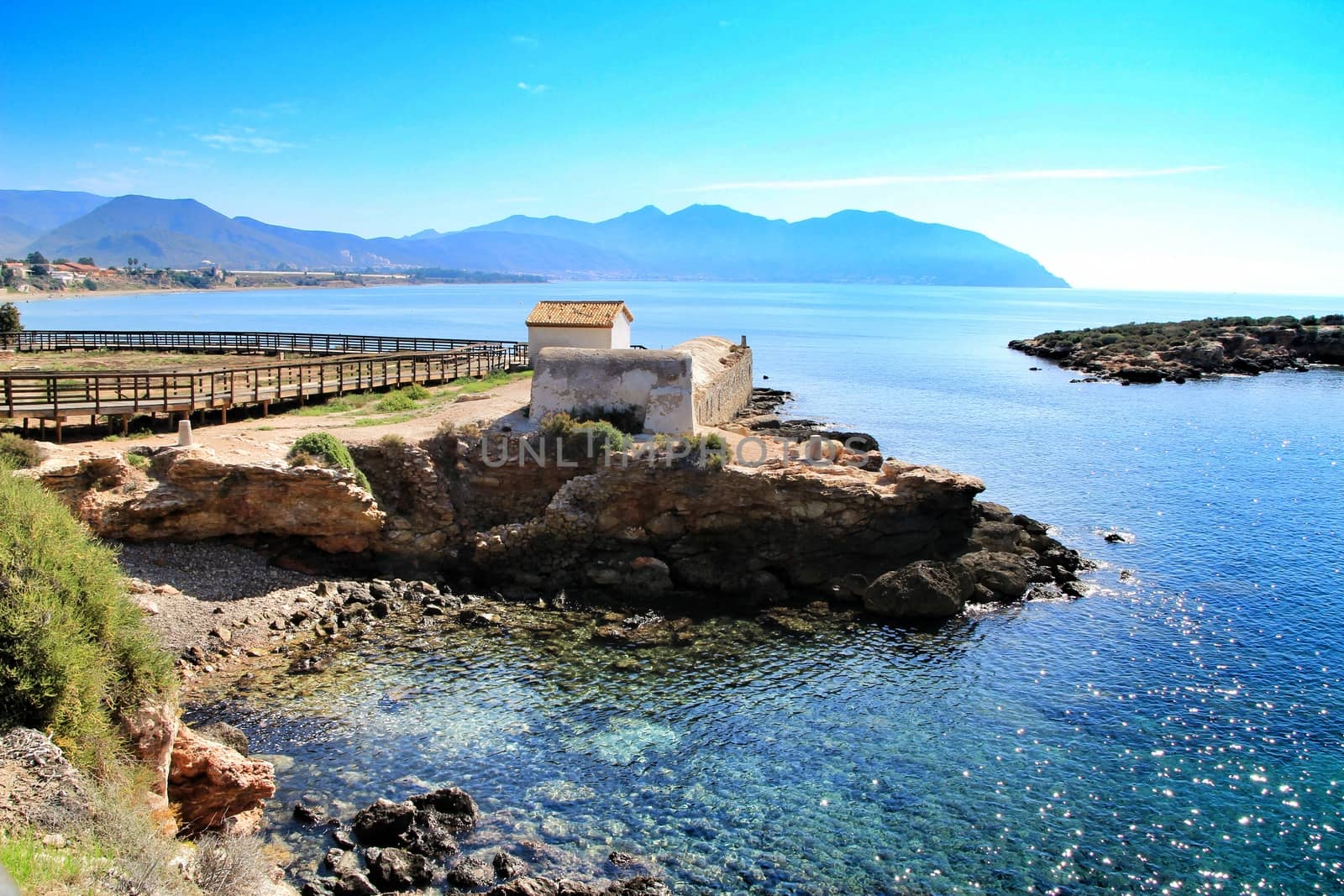 Old thermal baths on the beach with boulders, cliffs and mountains in Isla Plana village in Cartagena, Murcia, Spain in a sunny day