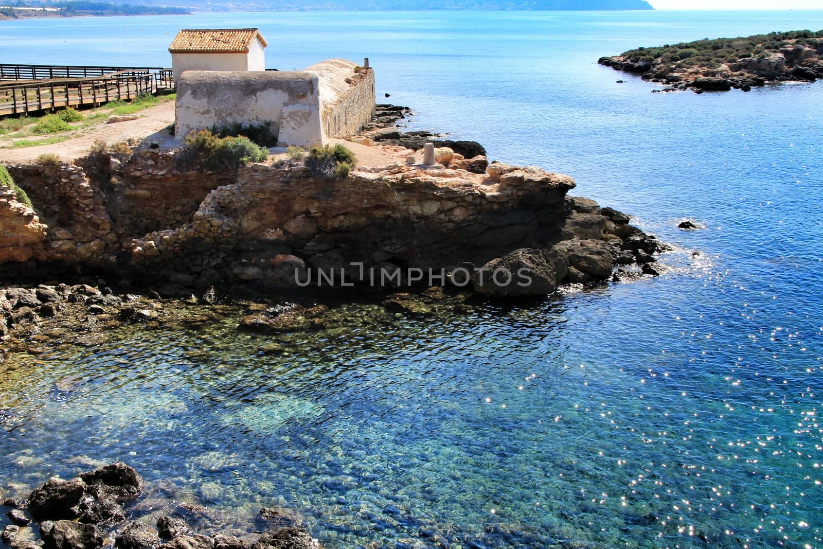 Old thermal baths on the beach with boulders, cliffs and mountains in Isla Plana village in Cartagena, Murcia, Spain in a sunny day