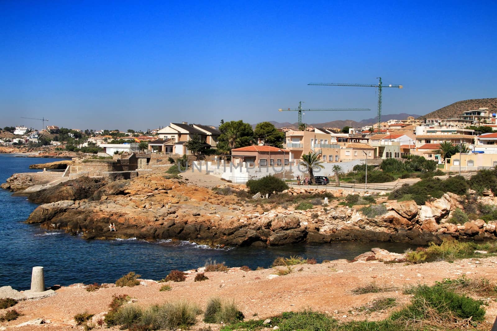 Beautiful beach with boulders, cliffs and mountains in Isla Plana village in Cartagena, Murcia, Spain in a sunny day