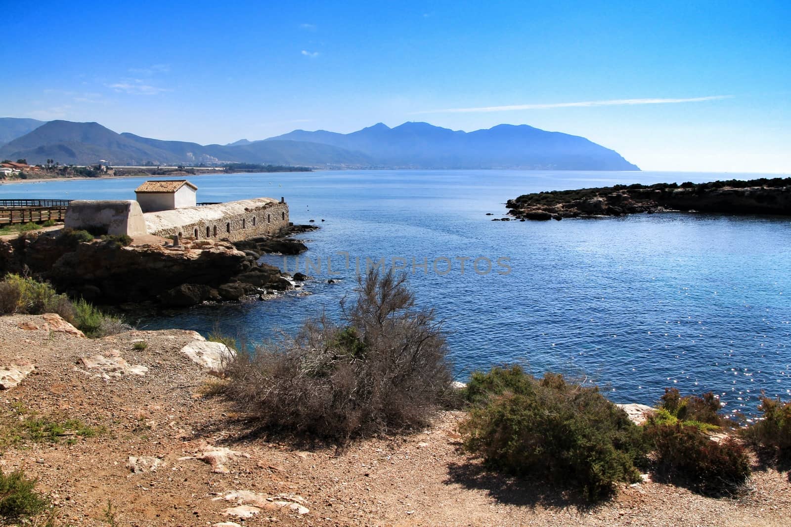 Beautiful beach with boulders, cliffs and mountains in Isla Plana village in Cartagena, Murcia, Spain in a sunny day