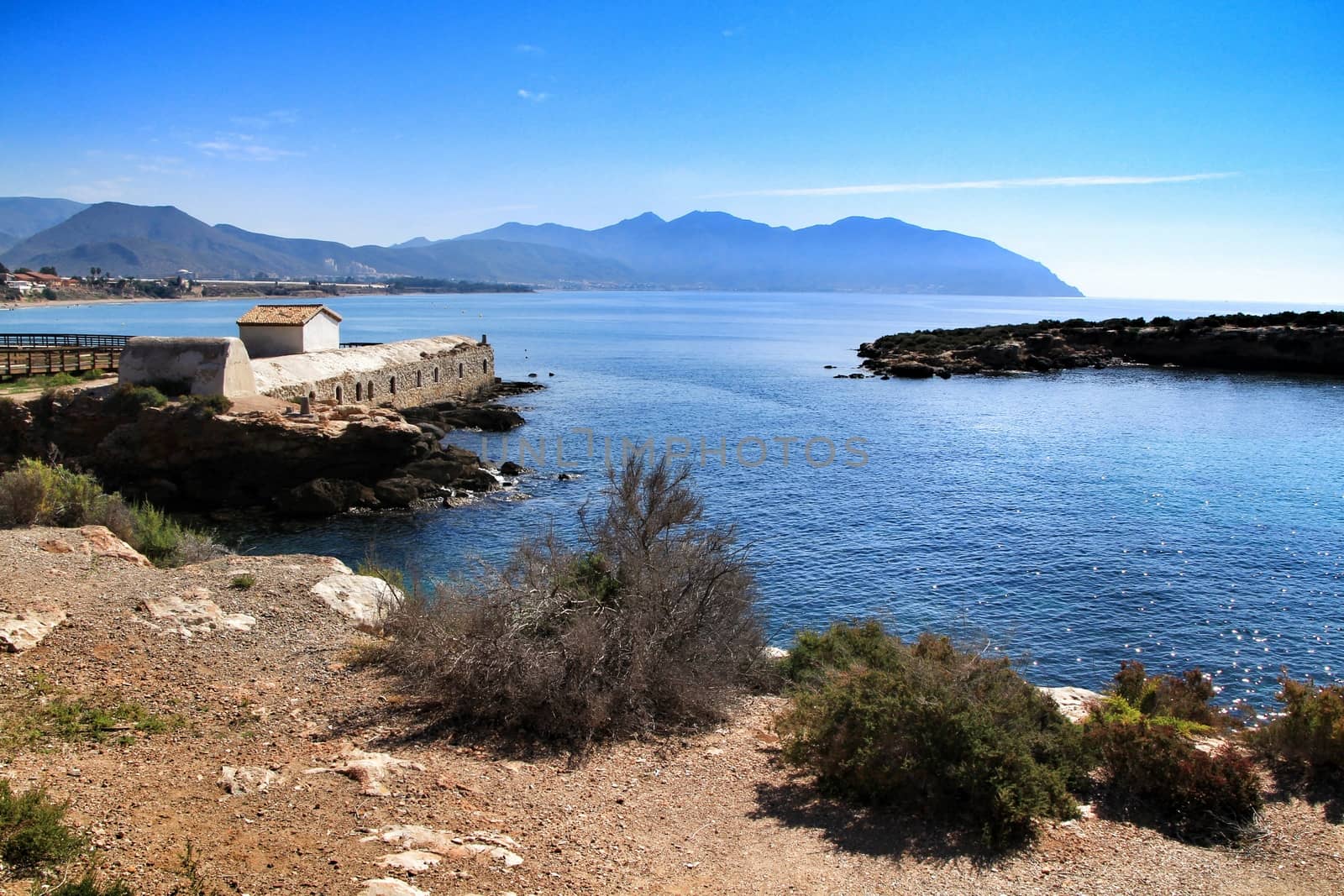 Beautiful beach with boulders, cliffs and mountains in Isla Plana village in Cartagena, Murcia, Spain in a sunny day