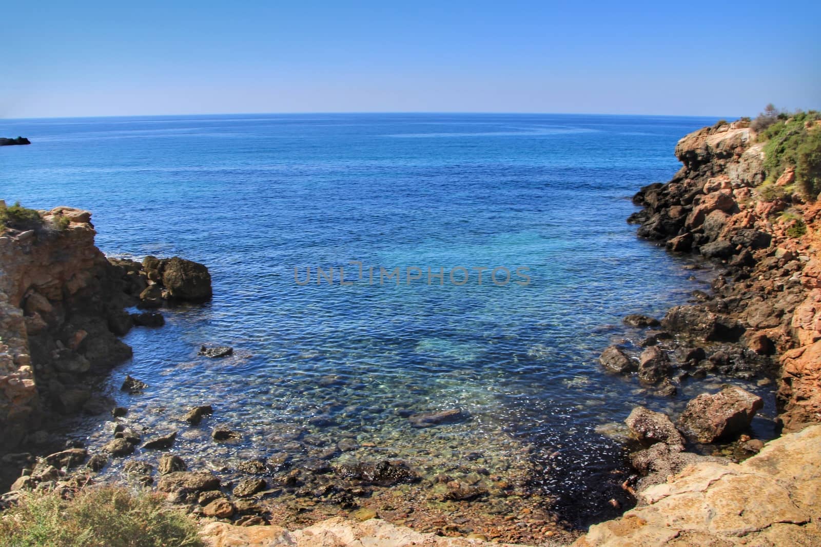 Beautiful beach with boulders, cliffs and mountains in Isla Plana village in Cartagena, Murcia, Spain in a sunny day