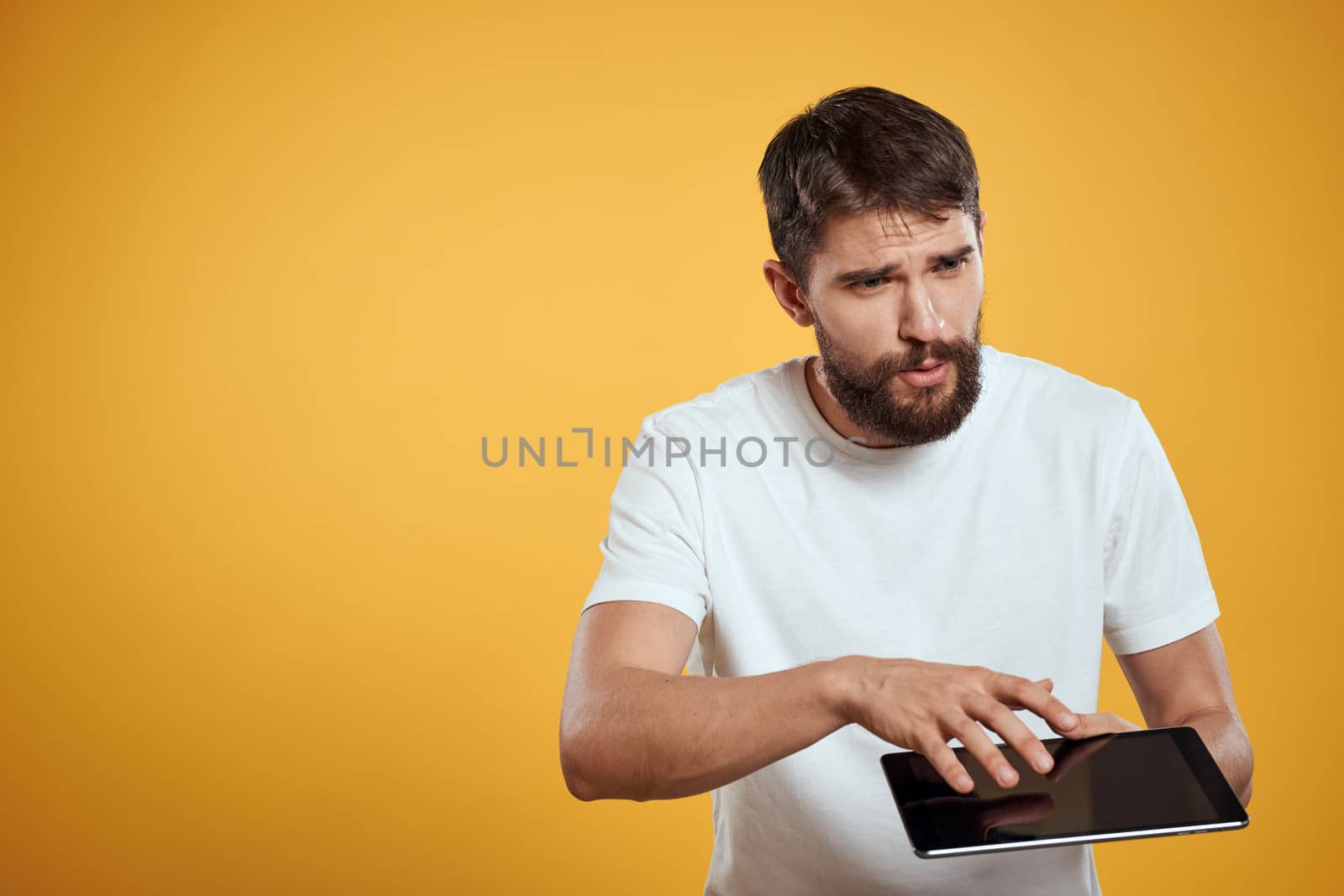 Man with a tablet on a yellow background in a white t-shirt new technologies businessman touch screen touchpad. High quality photo