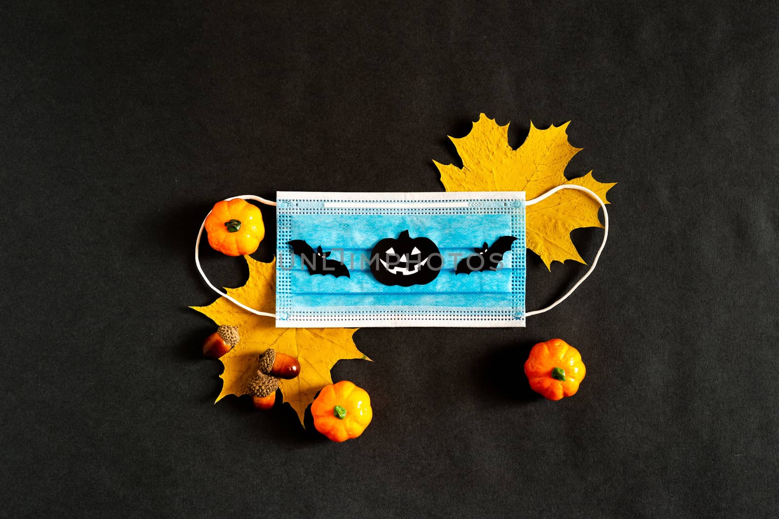 Halloween during the pandemic. Copy space. The view from the top. In the fall of 2020. Yellow maple leaves with a medical mask on a black background with black paper silhouettes, bat, pumpkin, spider by Pirlik