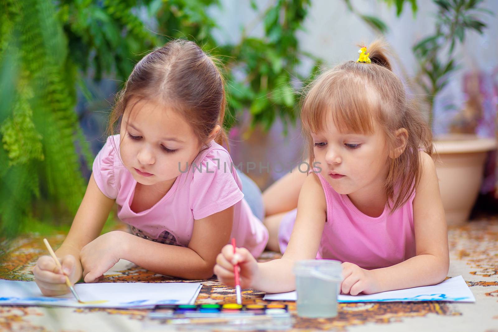 Two girls paint with paints lying on the floor at home or in kindergarten. Children's creativity