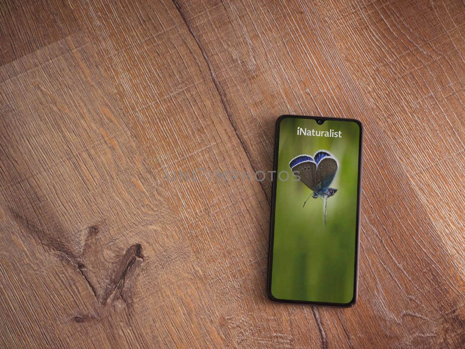 Lod, Israel - July 8, 2020: iNaturalist app launch screen with logo on the display of a black mobile smartphone on wooden background. Top view flat lay with copy space.