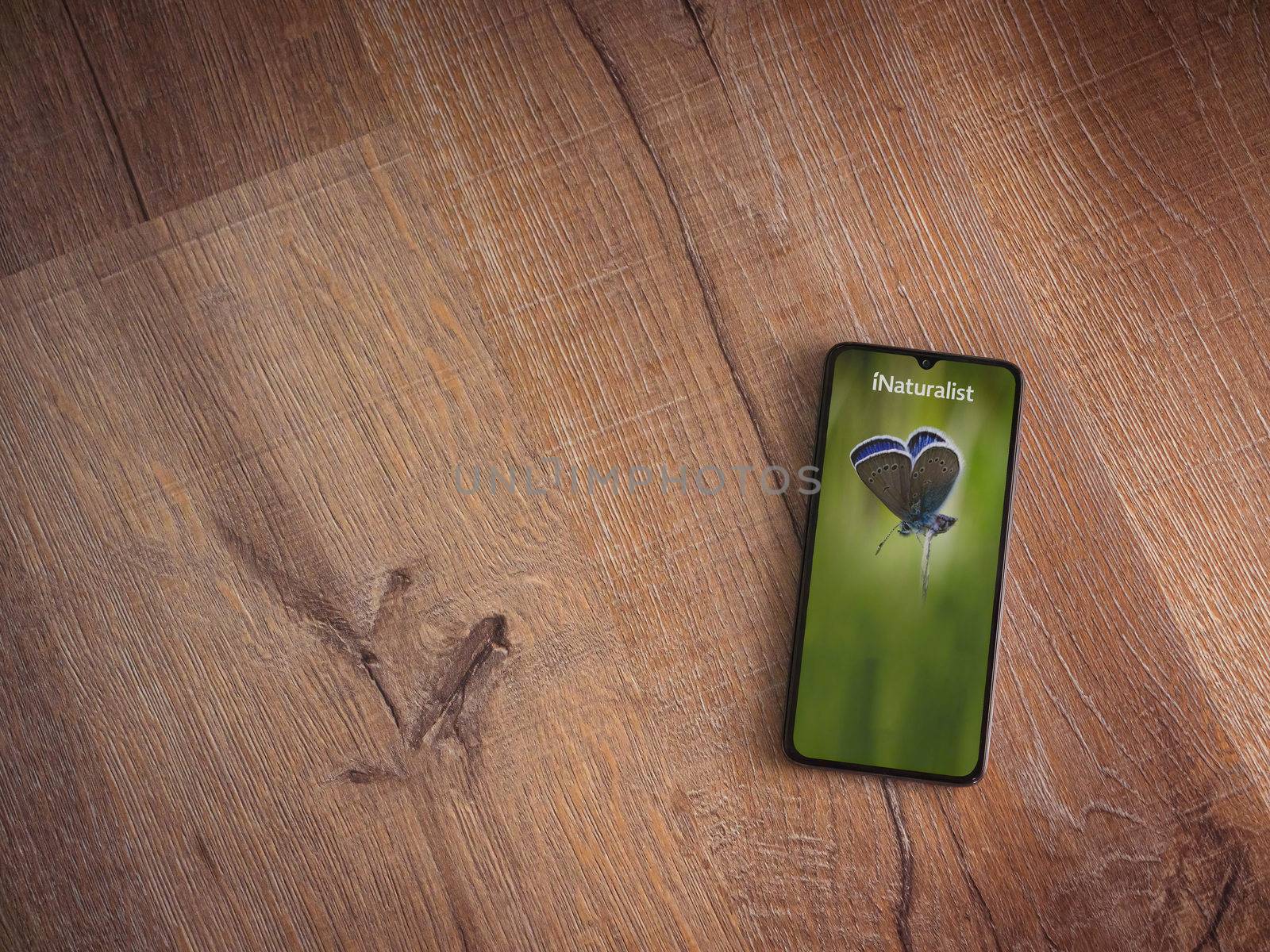 Lod, Israel - July 8, 2020: iNaturalist app launch screen with logo on the display of a black mobile smartphone on wooden background. Top view flat lay with copy space.
