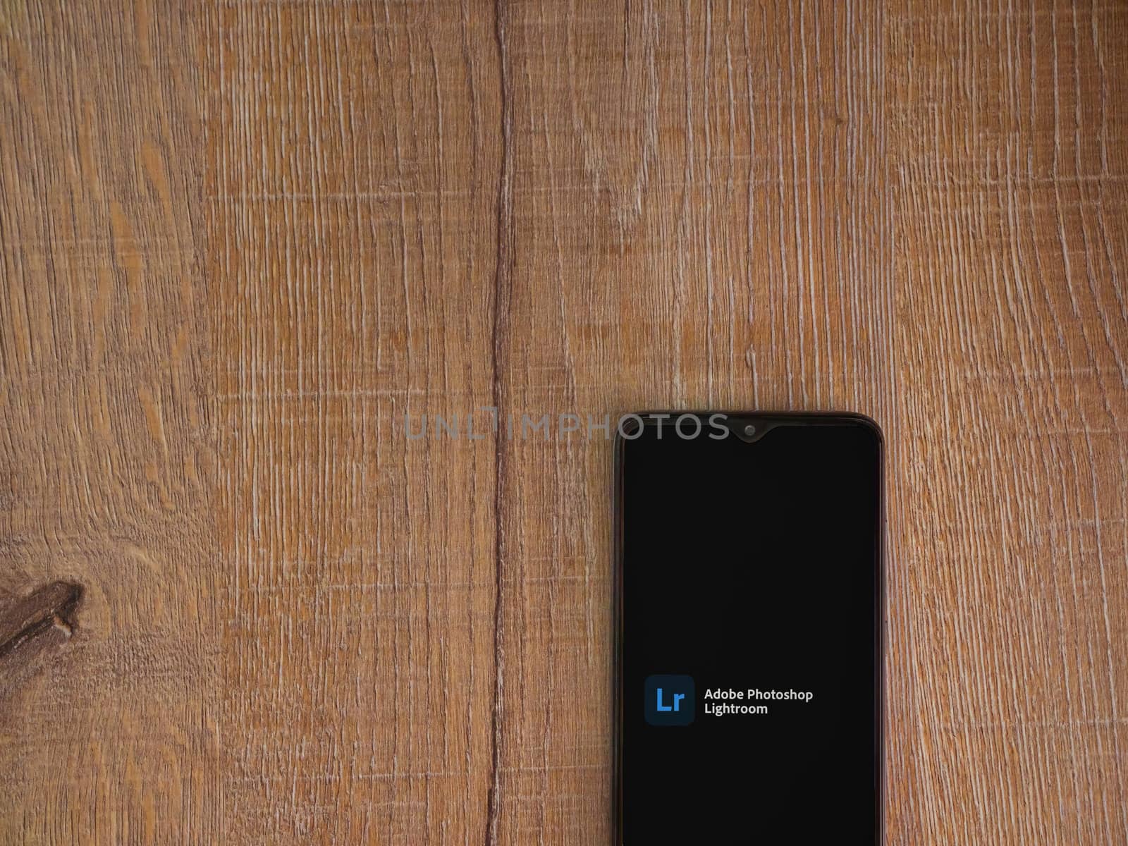 Lod, Israel - July 8, 2020: Adobe Lightroom - Photo Editor and Pro Camera app launch screen with logo on the display of a black mobile smartphone on wooden background. Top view flat lay with copy space.