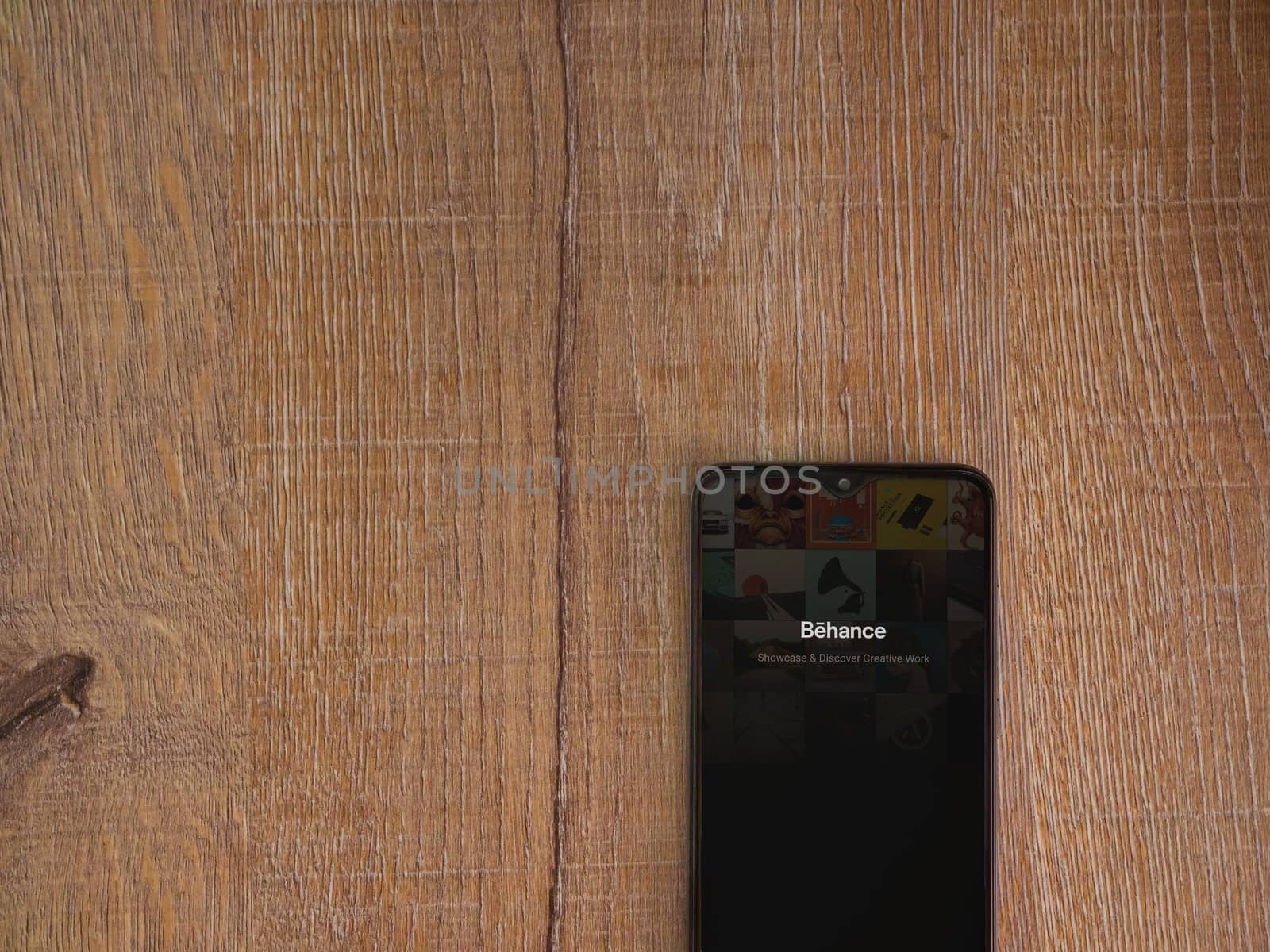 Lod, Israel - July 8, 2020: Adobe Behance app launch screen with logo on the display of a black mobile smartphone on wooden background. Top view flat lay with copy space. 