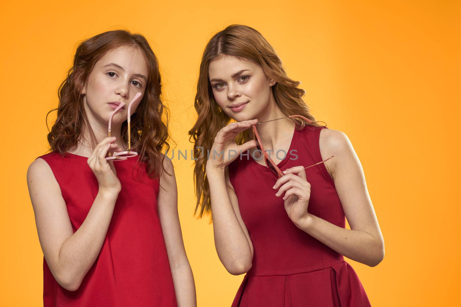Happy woman and little girl in red dress are having fun on a yellow background fashion emotions sisters fun gesturing with hands Copy Space. High quality photo