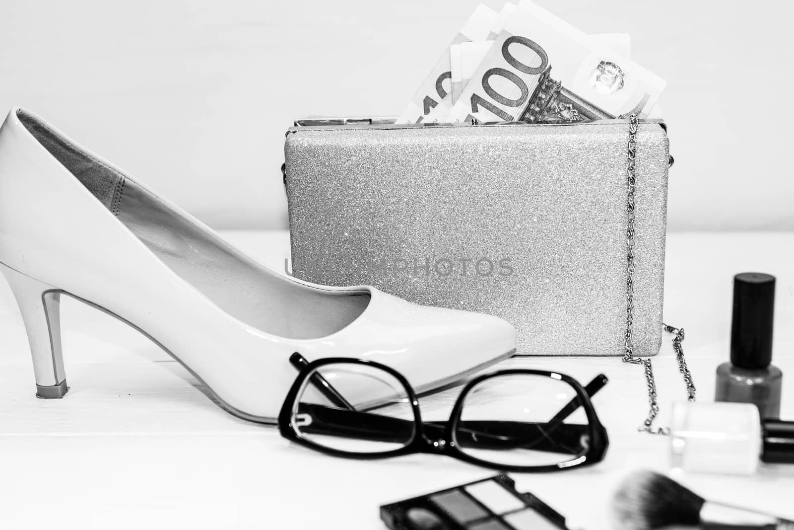 Glittery silver clutch bag with money and beauty products isolated on white background with copy space.