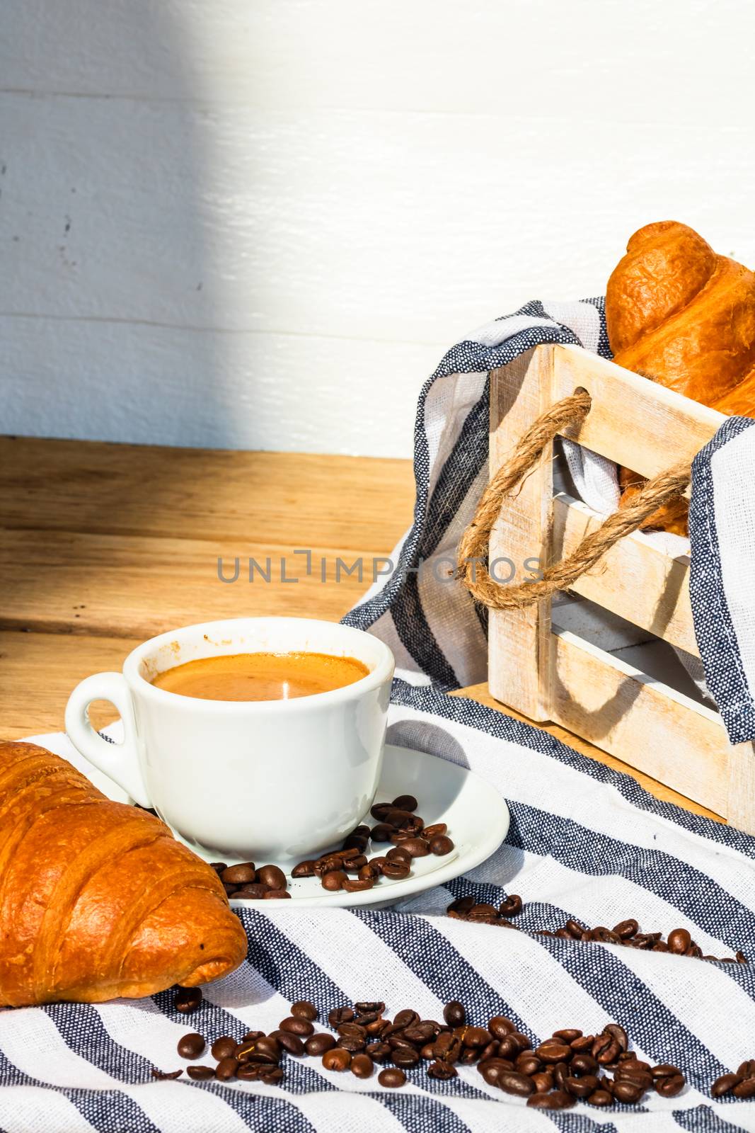 Puff pastry, coffee cup and buttered French croissant on wooden crate. Food and breakfast concept. Detail of coffee desserts and fresh pastries