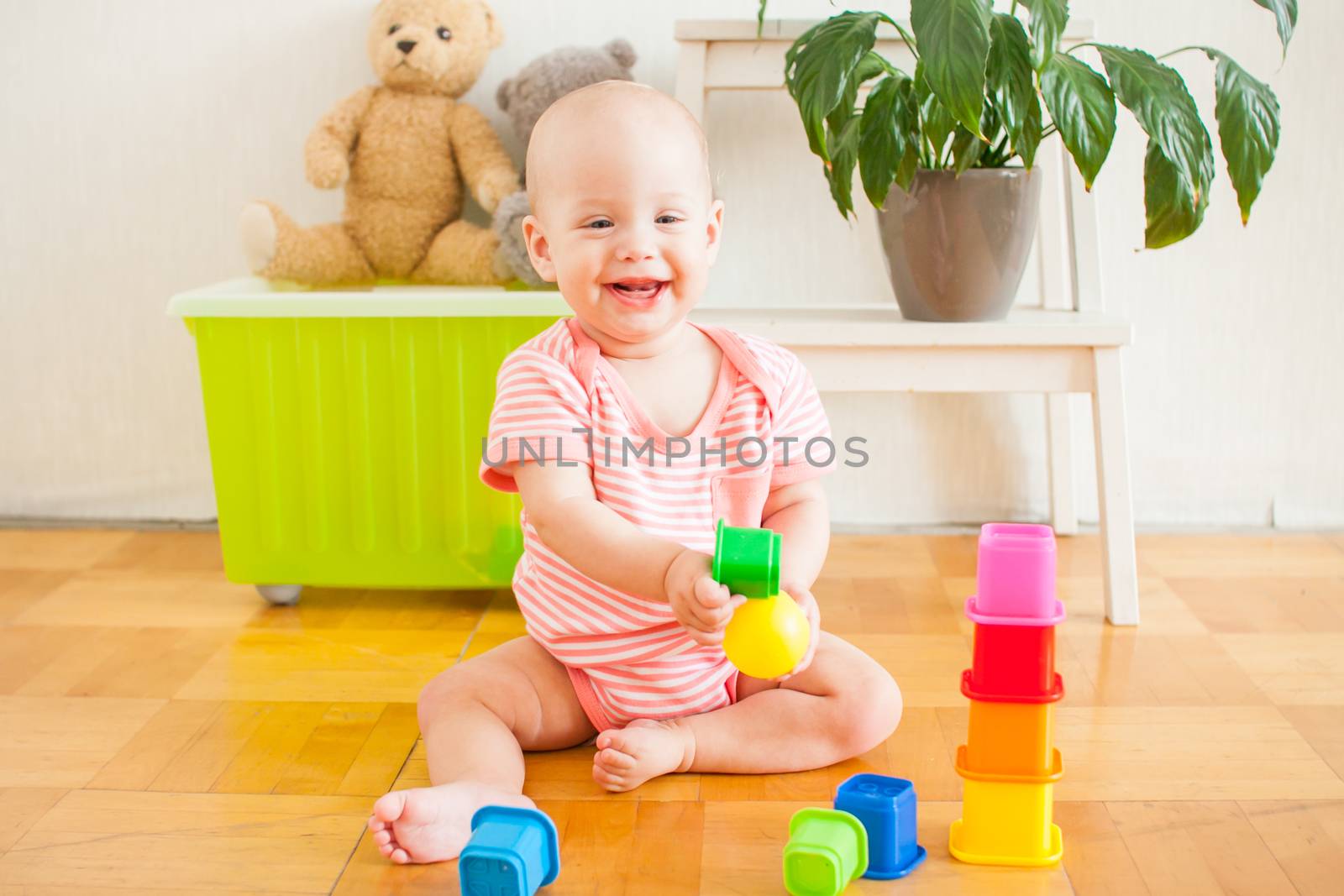 Little baby girl sitting on the floor, crawling and playing with brightly colored educational toys, pyramids