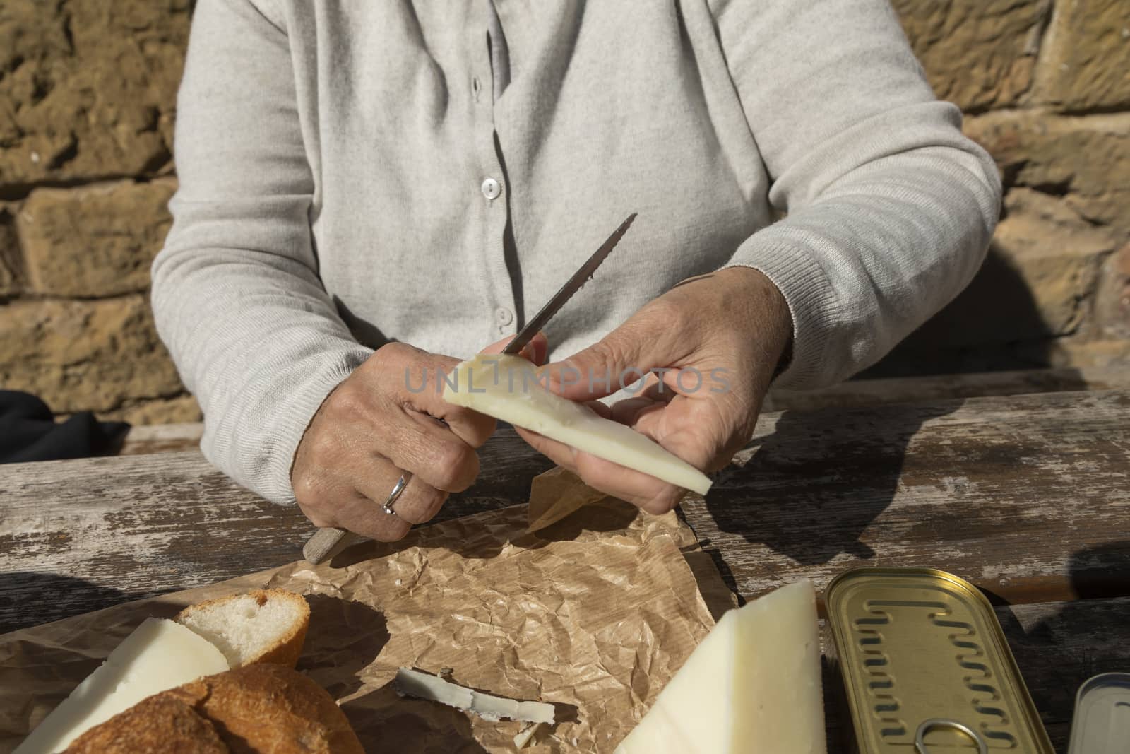 A senior woman, cuts slices of goat cheese, Spain by alvarobueno